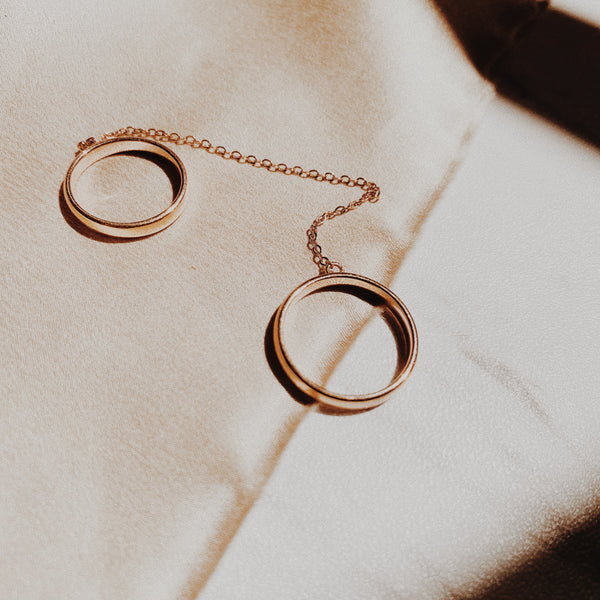 Two rose gold rings connected by a chain and can be worn on two different fingers or the same one. 